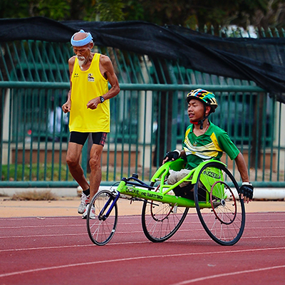 Wheelchair Athelete Running - Wheelchair Racing on Paralympic Track next to Elderly Man