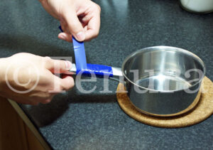 A person wraps a strip of blue Tenura grip roll around the metal handle of a saucepan to provide a heat-resistant, non-slip grip.