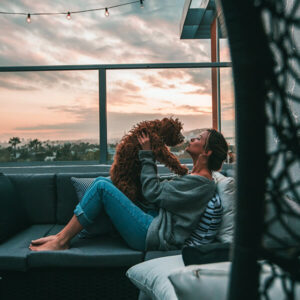 A woman bonding with a therapy dog on a balcony at sunset, highlighting the emotional support and companionship benefits of assisted therapy dogs.