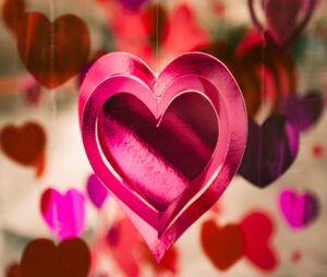 A shiny pink heart-shaped decoration hanging among several other blurred red and pink hearts in the background.
