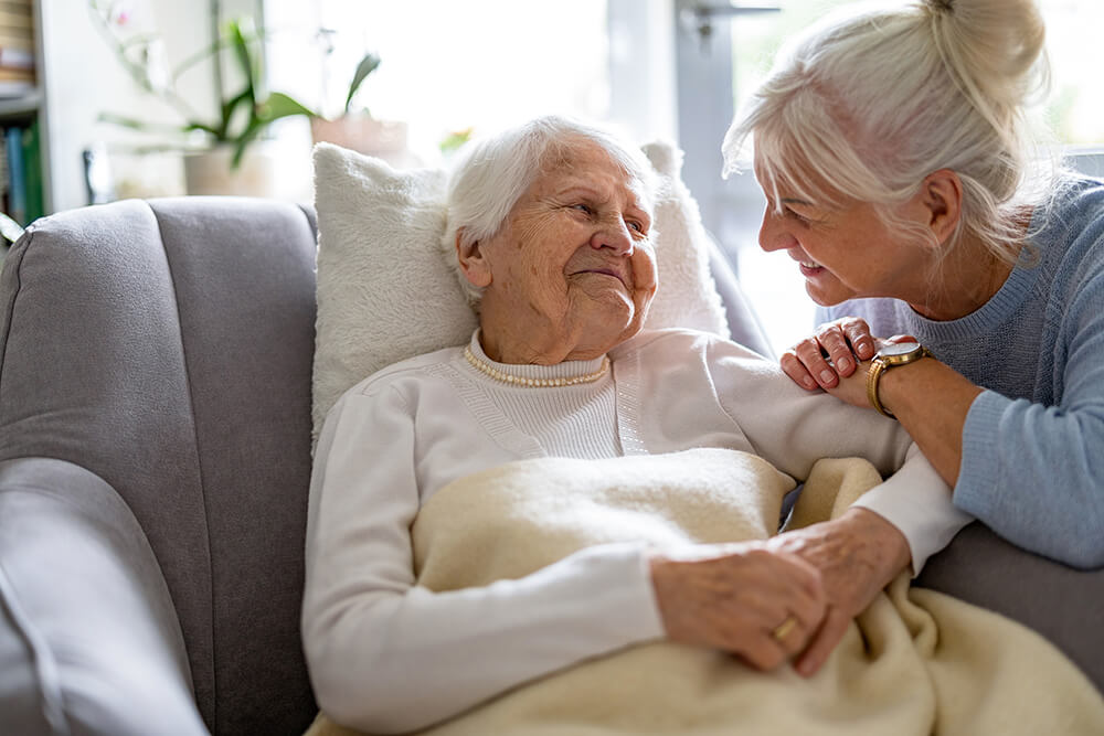 Smiling female caregiver comforting an elderly woman at home, symbolising trust and emotional support in senior care.