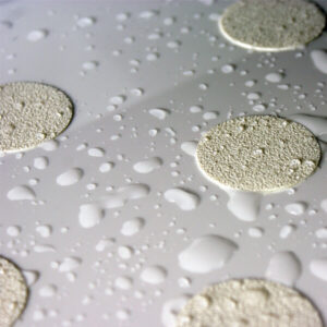 Close-up of white textured circular anti-slip stickers on a wet bathroom surface, designed to prevent slipping in showers or bathtubs.