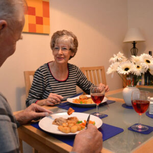 Smiling elderly couple having dinner at a table with blue anti-slip placemats under their plates and glasses.