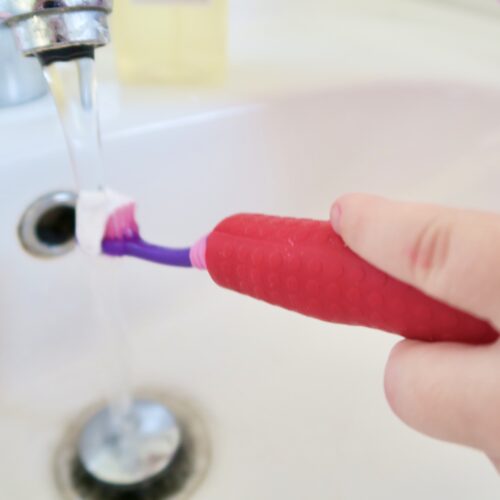 T-PCG-R-Red-Childrens-Cutlery-Grips-Girl-Holding-Toothbrush-Under-Tap-1
